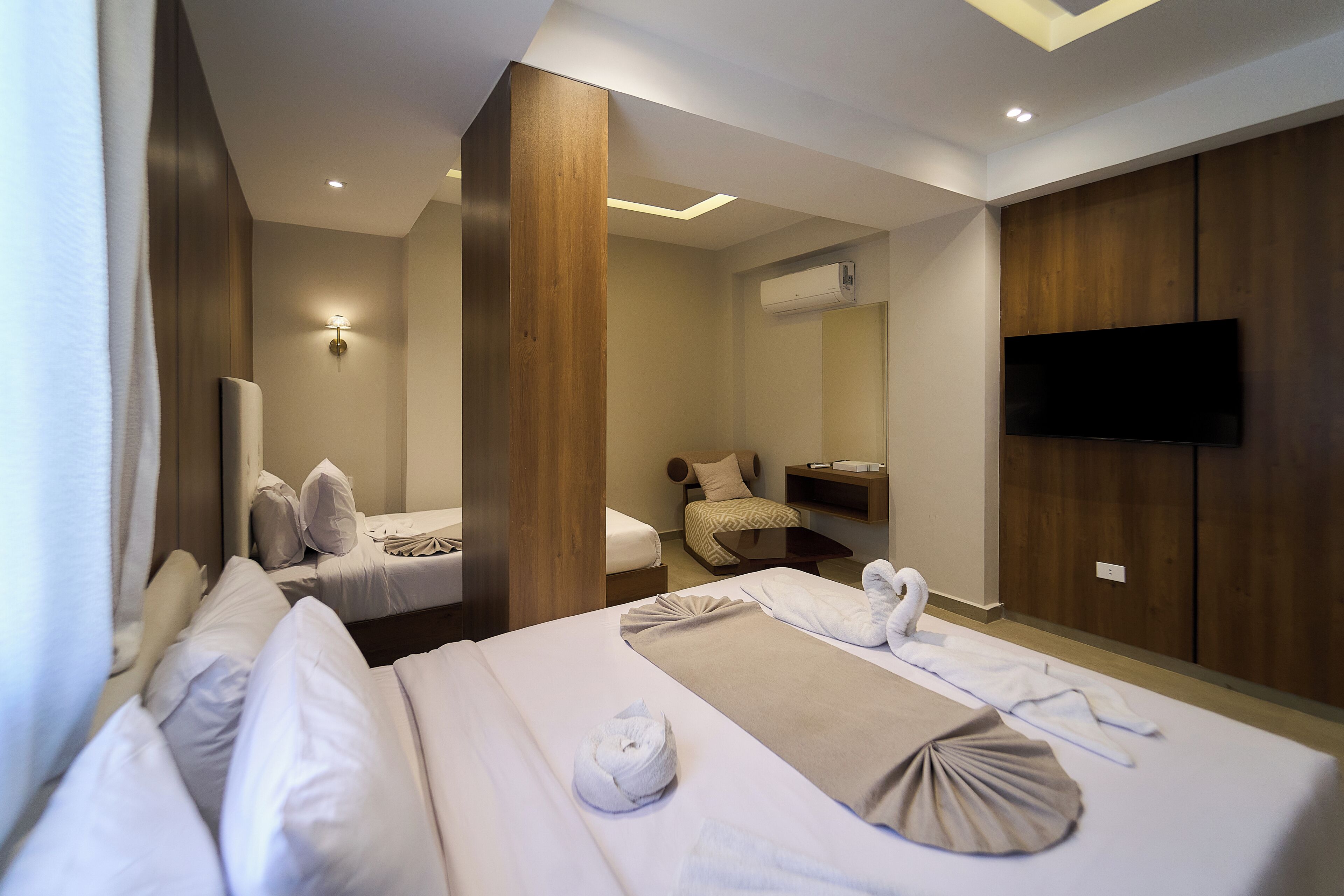 A hotel room with two beds, a flat-screen TV, a wall-mounted air conditioner, and a large mirror.