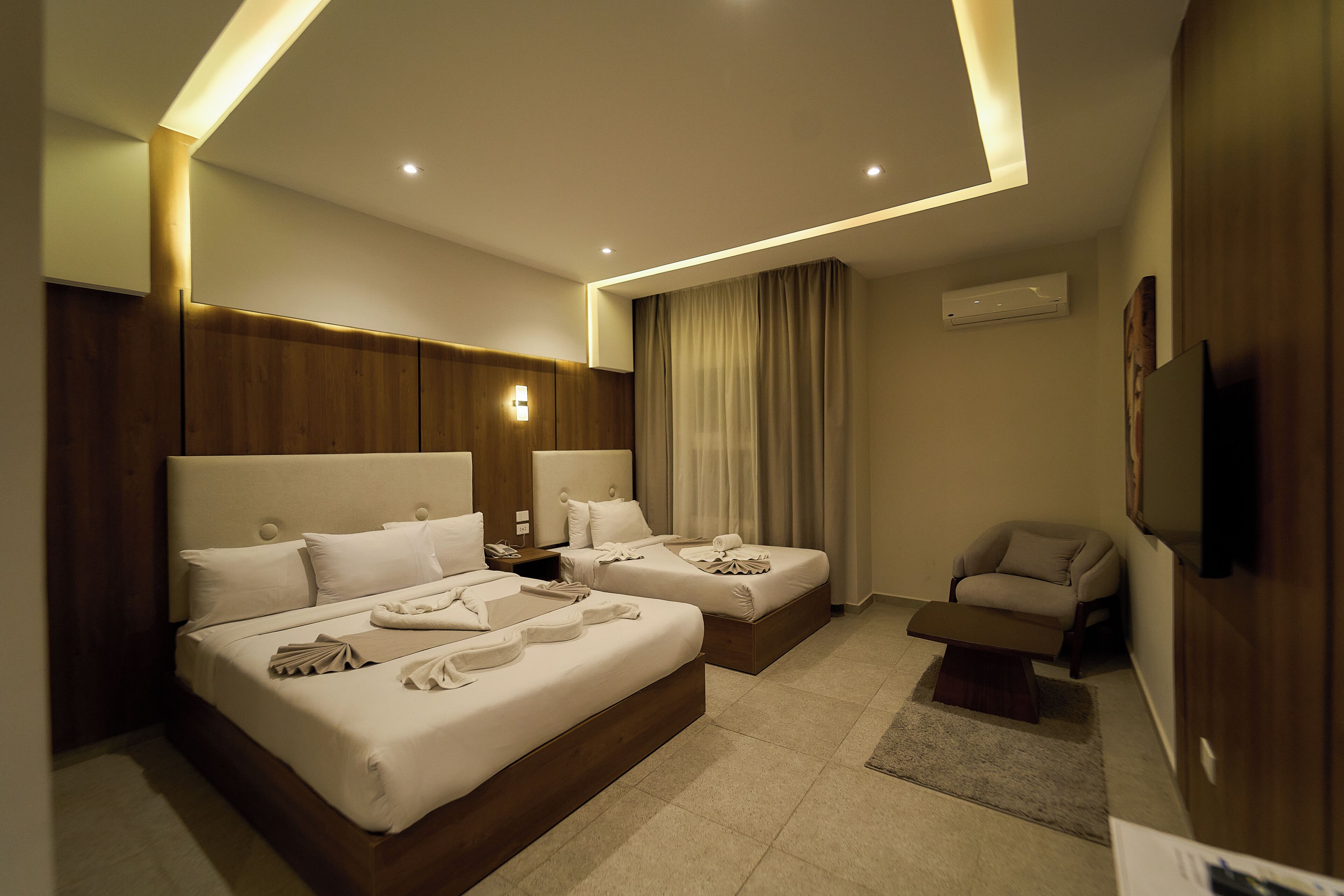 A hotel room with two beds, a sitting area, and a flat-screen TV.
