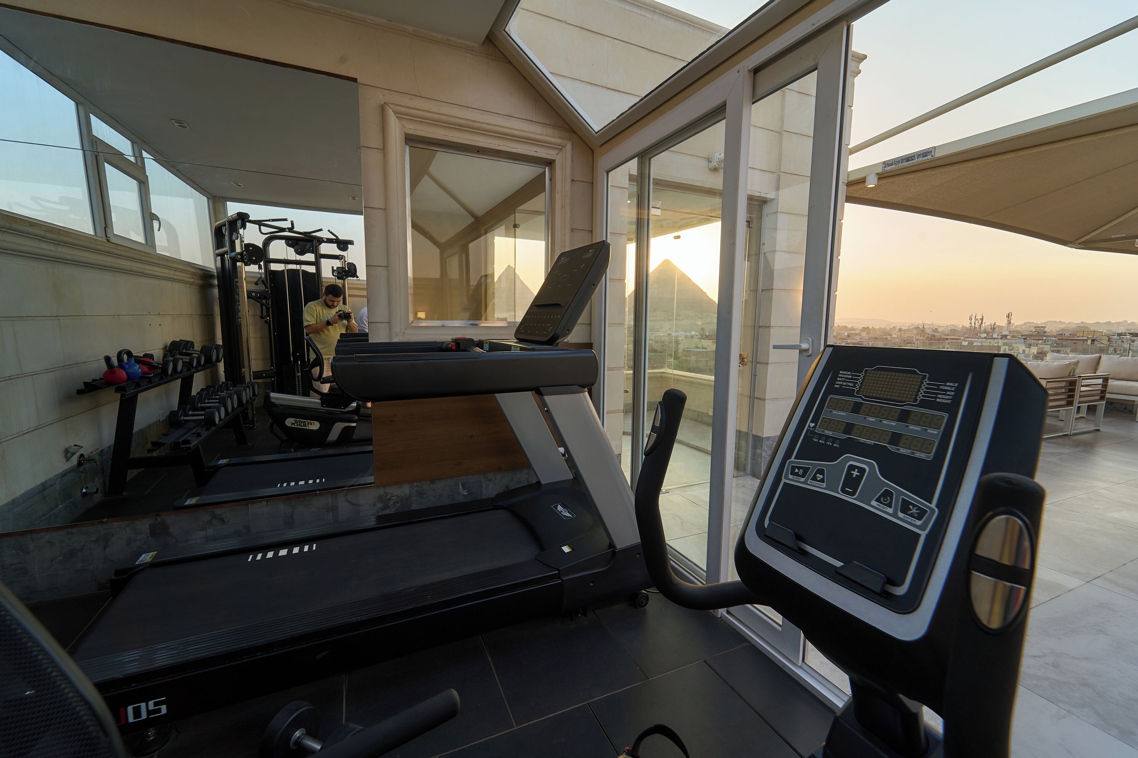 A gym with exercise equipment, a treadmill, and a view of a cityscape through large windows.