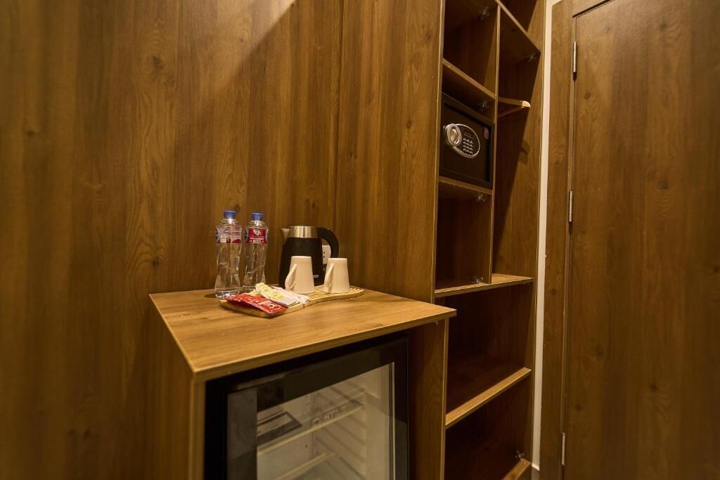 A wooden-framed minibar with a glass door, containing bottled water, a coffee maker, and a small tray with snacks.