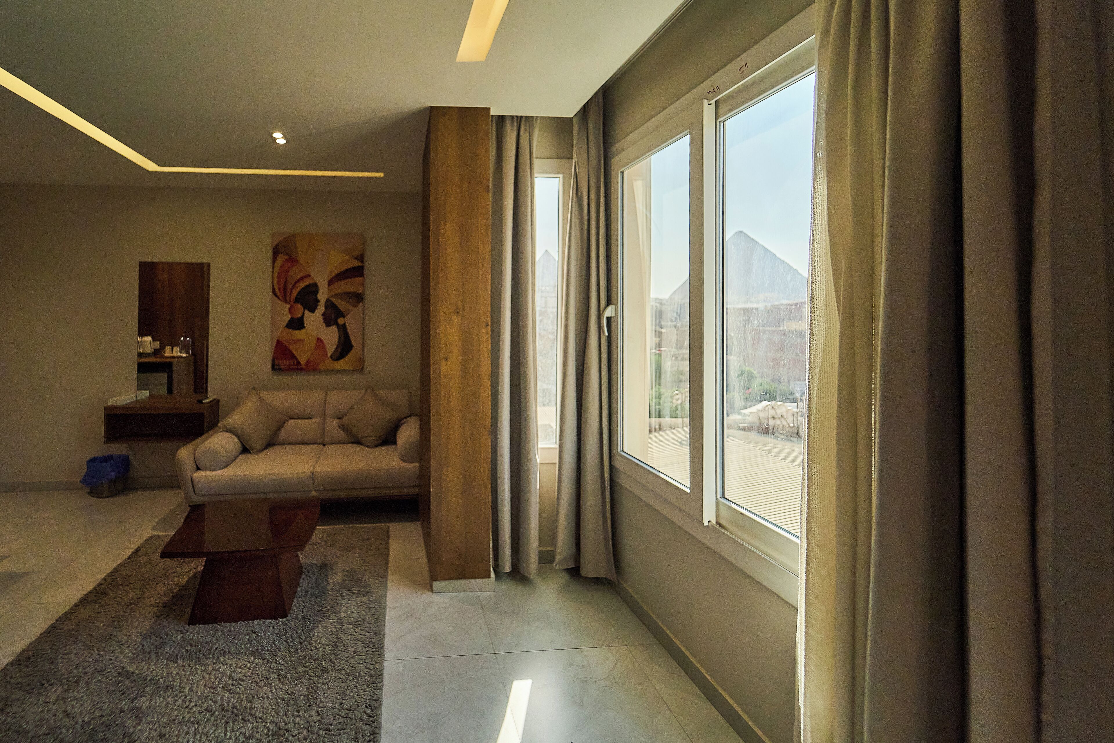 Ein modernes Wohnzimmer mit einem großen Fenster, einem Sofa, einem Couchtisch und einem Gemälde an der Wand.