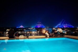 A poolside area with a view of illuminated pyramids in the background. - Kemet Pyramids View Hotel (Giza)