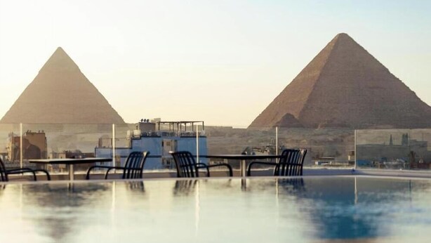 A rooftop bar with tables and chairs, overlooking two pyramids. - Kemet Pyramids View Hotel (Giza)