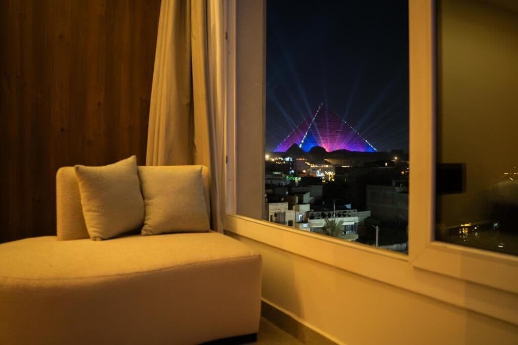 A room with a sofa, a window with a view of a cityscape and a lit structure.