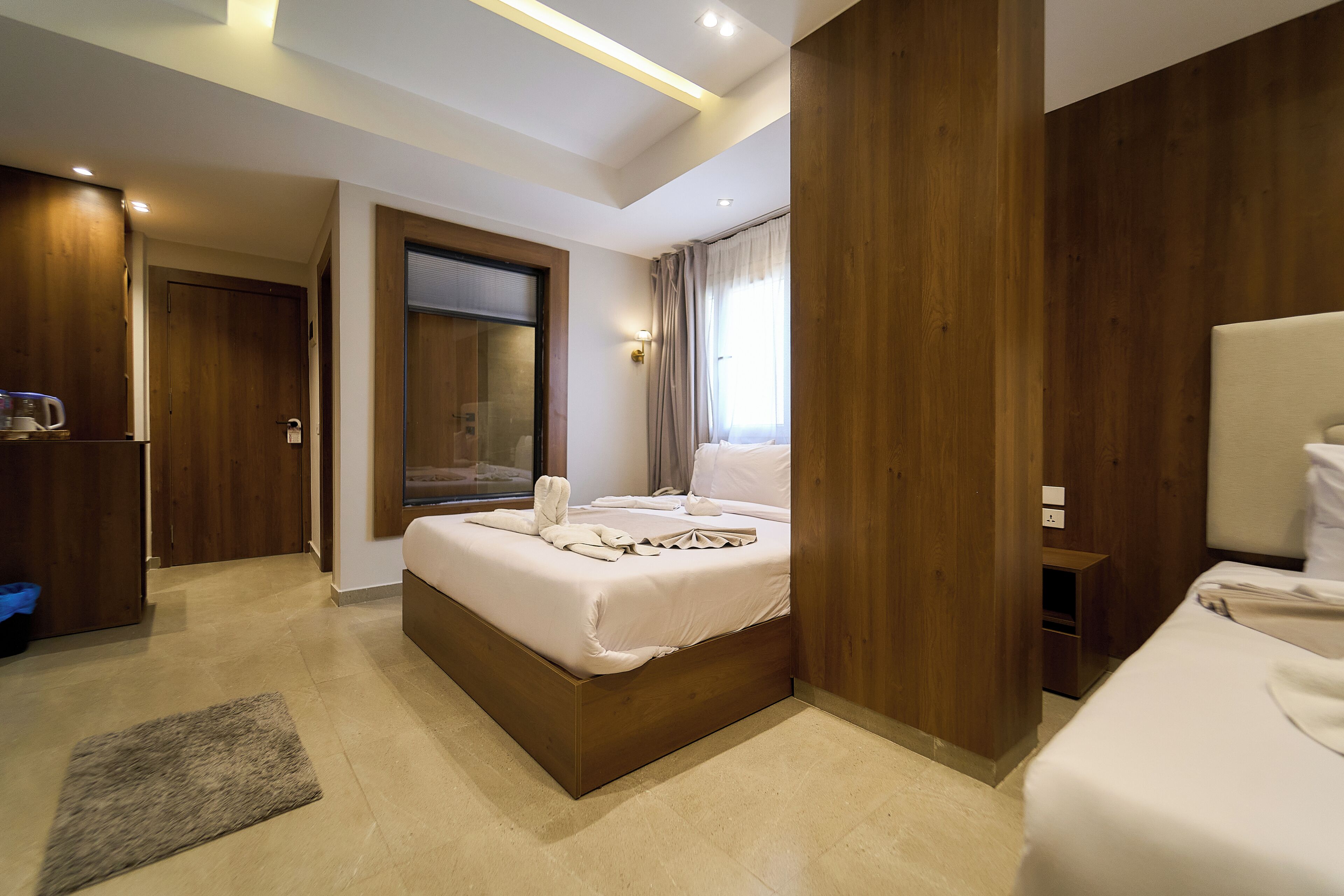A hotel room with a large bed, a wooden wardrobe, a bathroom with a mirror, and a small bedside table.