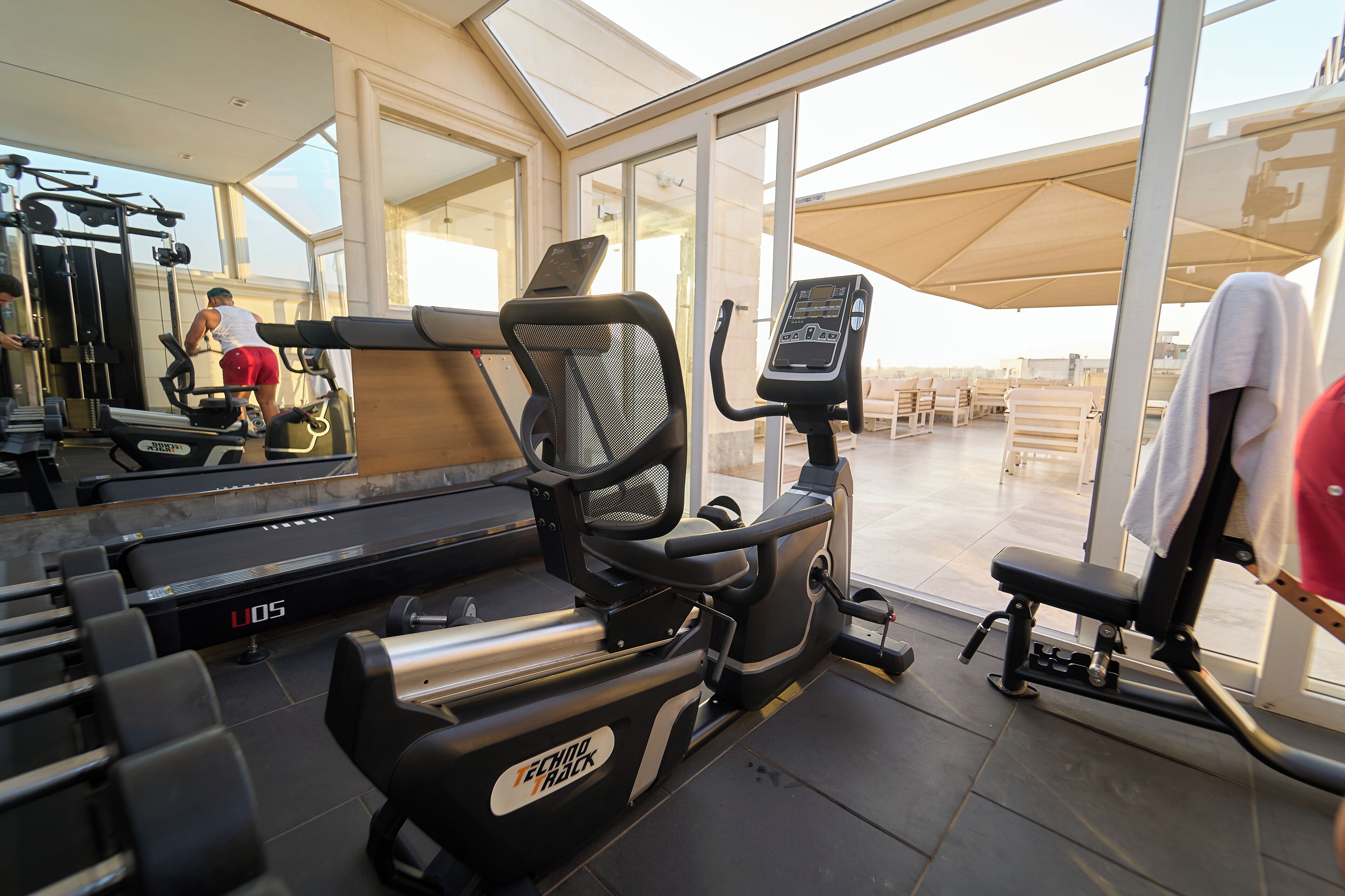 Un gimnasio con equipo cardiovascular, un espejo y vistas al exterior.