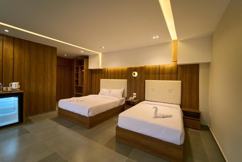 A modern hotel room with two beds, a desk, and a wardrobe.