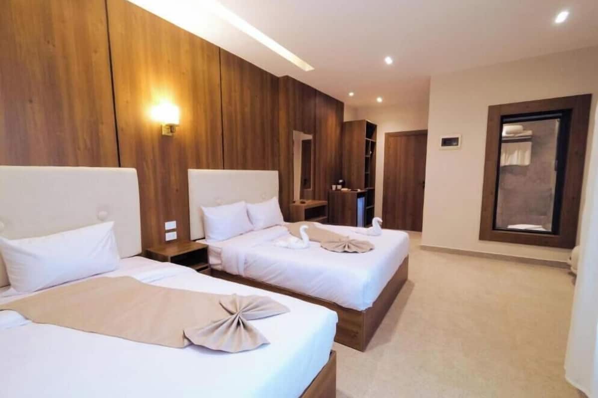Hotellihuone, jossa on kaksi sänkyä, puupanelointi, peili ja ikkuna.