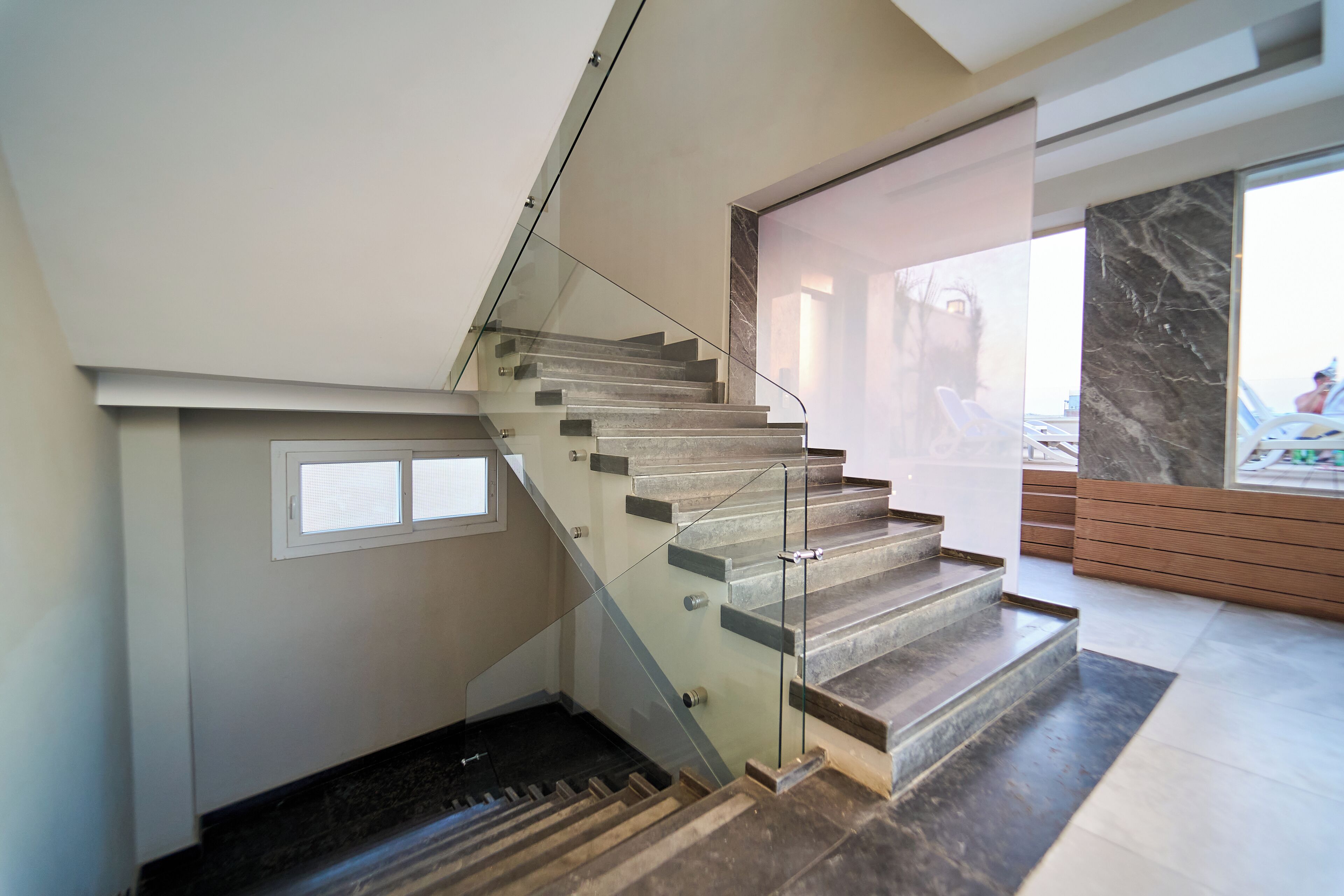 A modern staircase with glass railings and a marble floor.