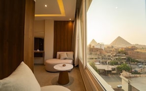 Ein modernes Hotelzimmer mit Blick auf die Pyramiden, einer Couch, einem kleinen Tisch und einer Wand mit Holzverkleidung.