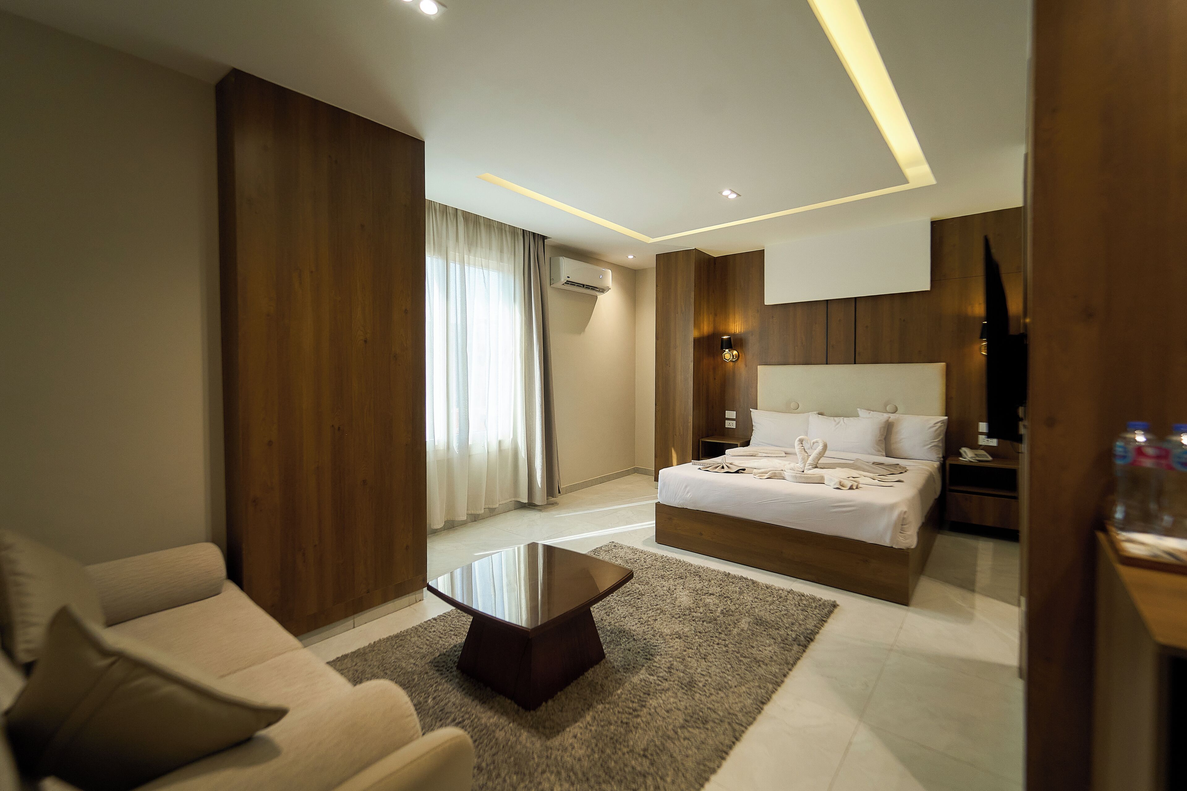A modern hotel room with a large bed, a sofa, a coffee table, and a TV.