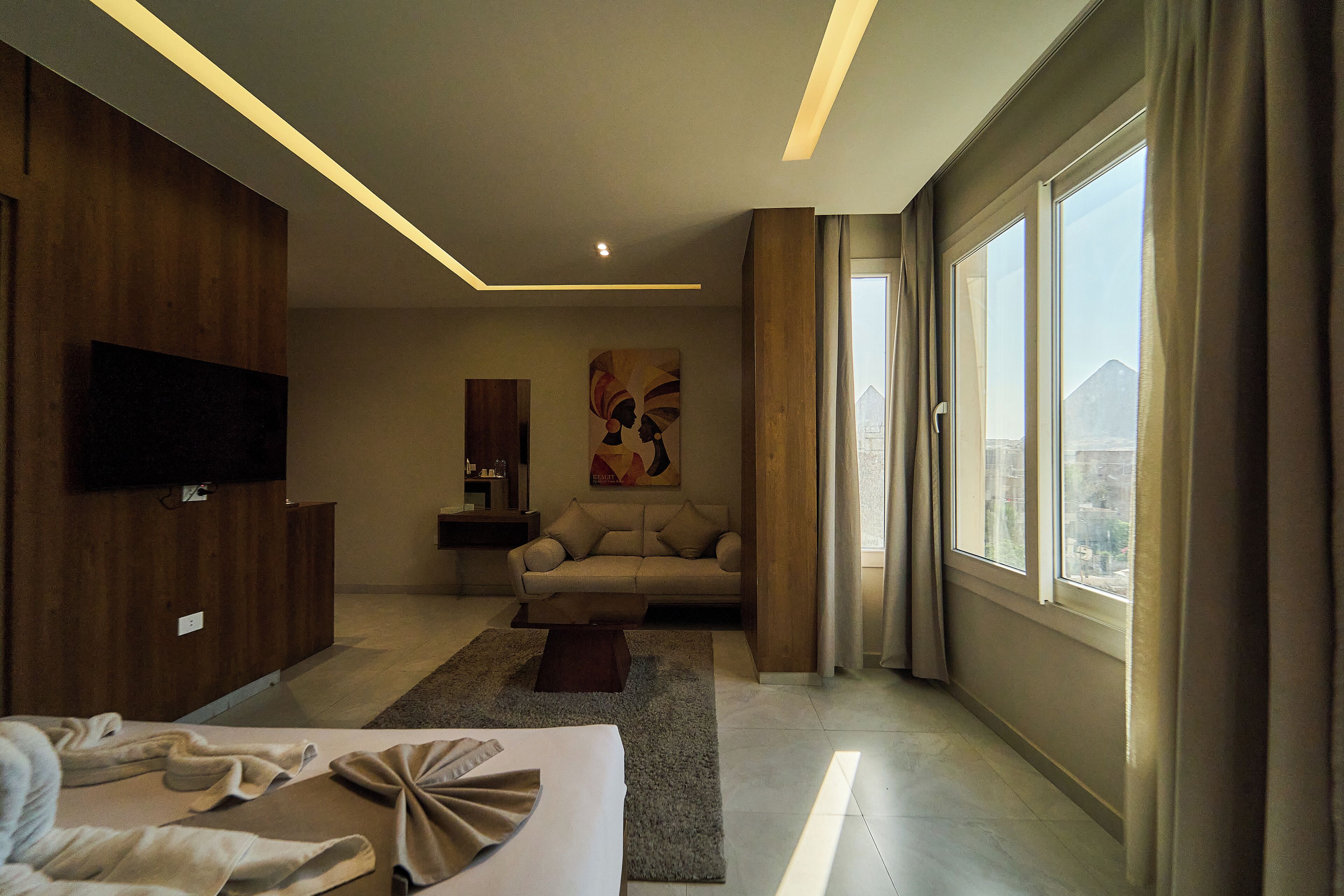 A modern hotel room with a large bed, a sofa, a TV mounted on the wall, and a painting.