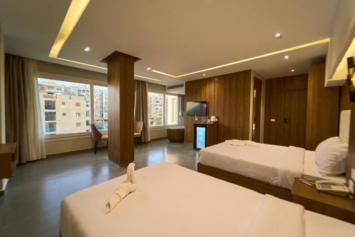 Habitación de hotel con dos camas, televisión, escritorio y vistas a edificios.