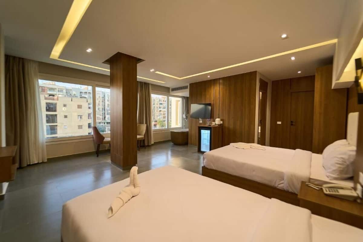 Habitación de hotel con dos camas, televisión, escritorio y vistas a edificios.