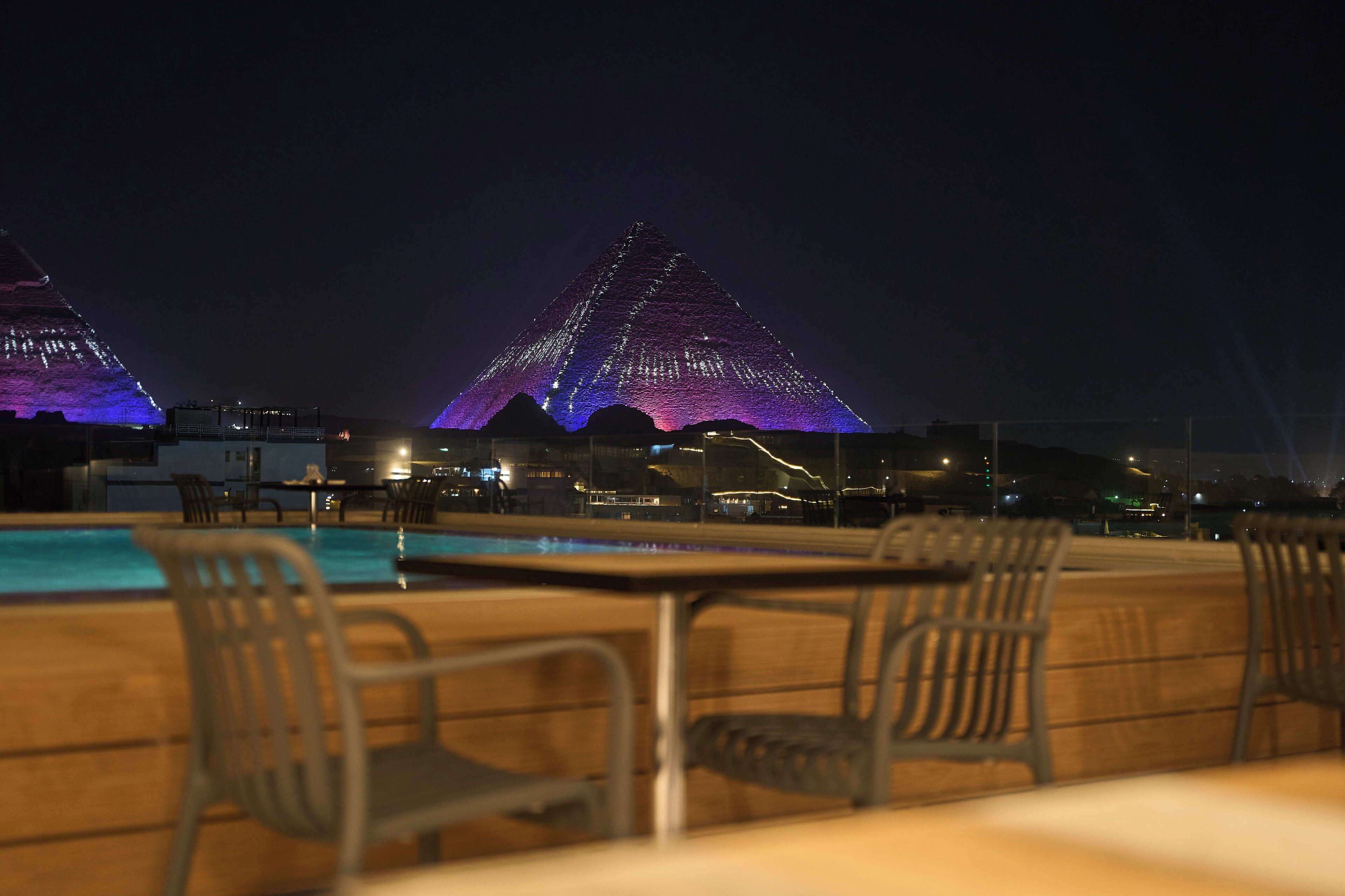 A nighttime view of a swimming pool area with two illuminated pyramids in the background.