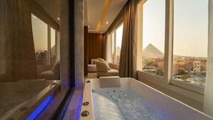 A modern bathroom with a bathtub, large windows, and a view of a pyramid. - Kemet Pyramids View Hotel (Giza)