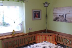 Een kamer met een houten bank, een raam met gordijn, een wandlamp en een ingelijste foto.