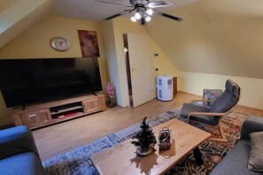 Een woonkamer met een flatscreen televisie, een plafondventilator, een houten salontafel, een bank en een stoel.