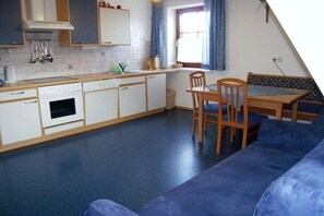 A compact kitchen with a dining area, a blue sofa, and a window with curtains.