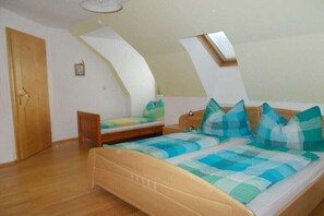Un dormitorio con techo inclinado, una cama con ropa de cama a cuadros, una mesita de noche pequeña y una ventana.