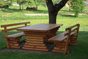 Una mesa de picnic de madera con bancos, rodeada de césped y árboles.