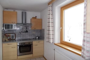 Eine kompakte Küche mit Mikrowelle, Backofen und einem Fenster mit Vorhängen.