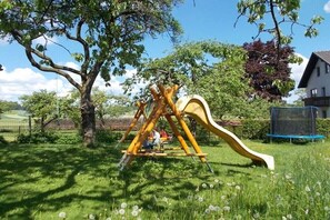 Une aire de jeux avec un toboggan et une structure d’escalade, entourée d’arbres et d’herbe.