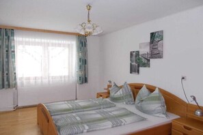 Une chambre à coucher avec un lit, des rideaux, une table de chevet, une lampe et des œuvres d’art murales.