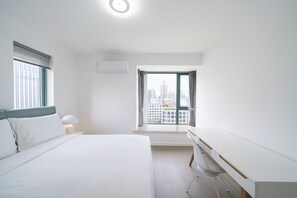 A modern hotel room with a bed, desk, and a large window offering a city view. - Tyms 3BR 2BA Family Serviced Apt (Shanghai)