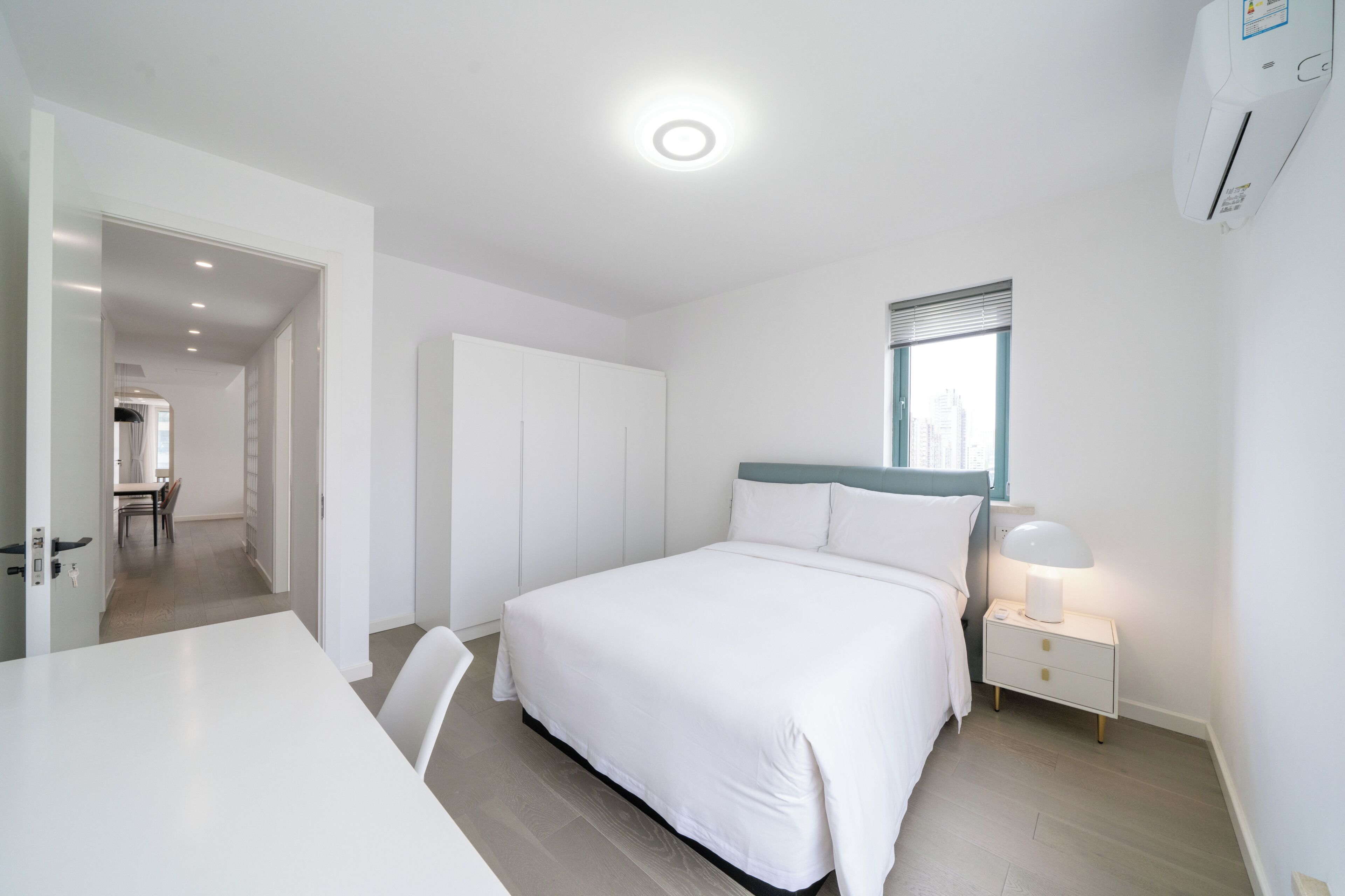 A bedroom with a bed, bedside table, lamp, and a window with blinds.