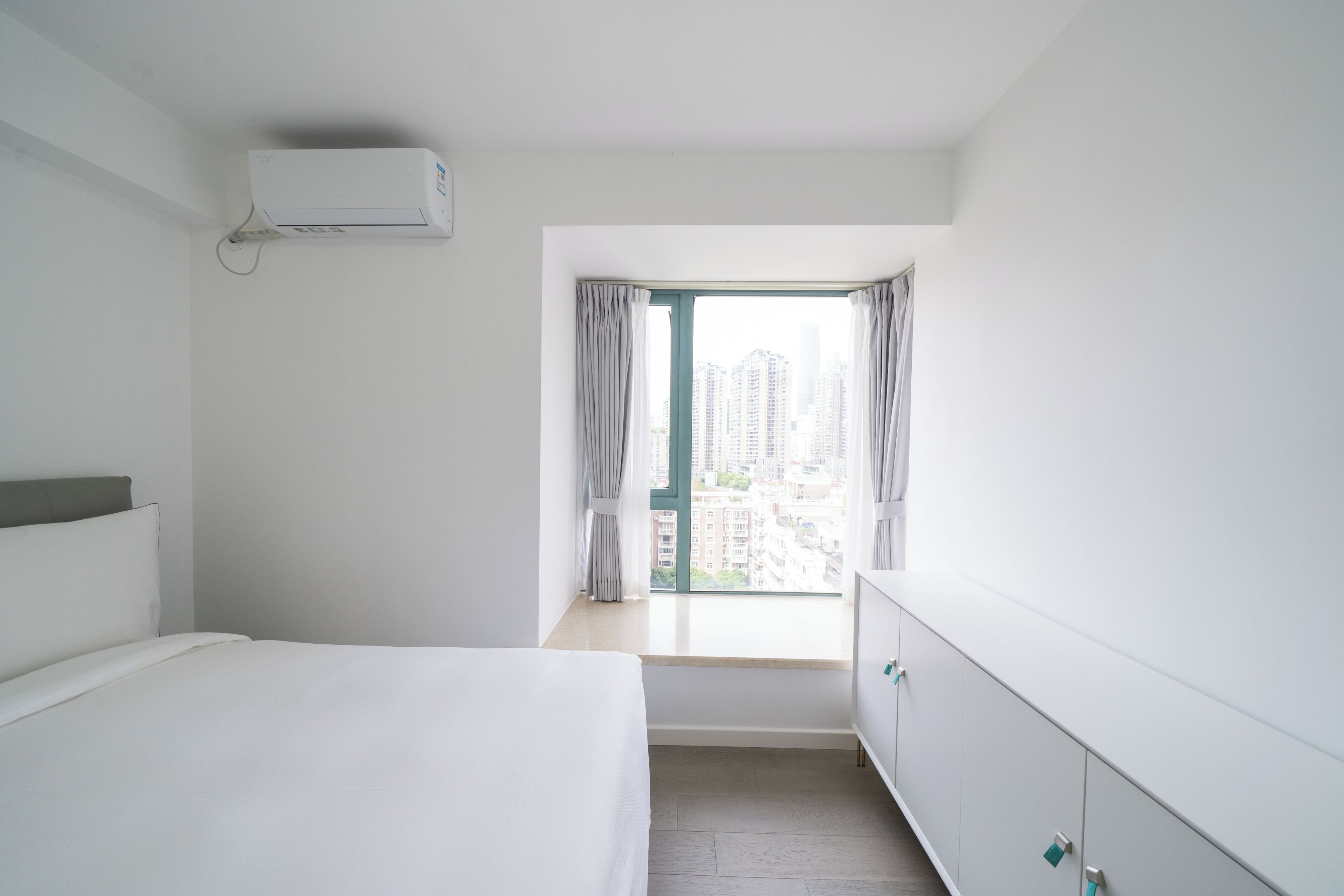 Une chambre d’hôtel comprenant un lit, une fenêtre avec des rideaux, une armoire et un appareil de climatisation.