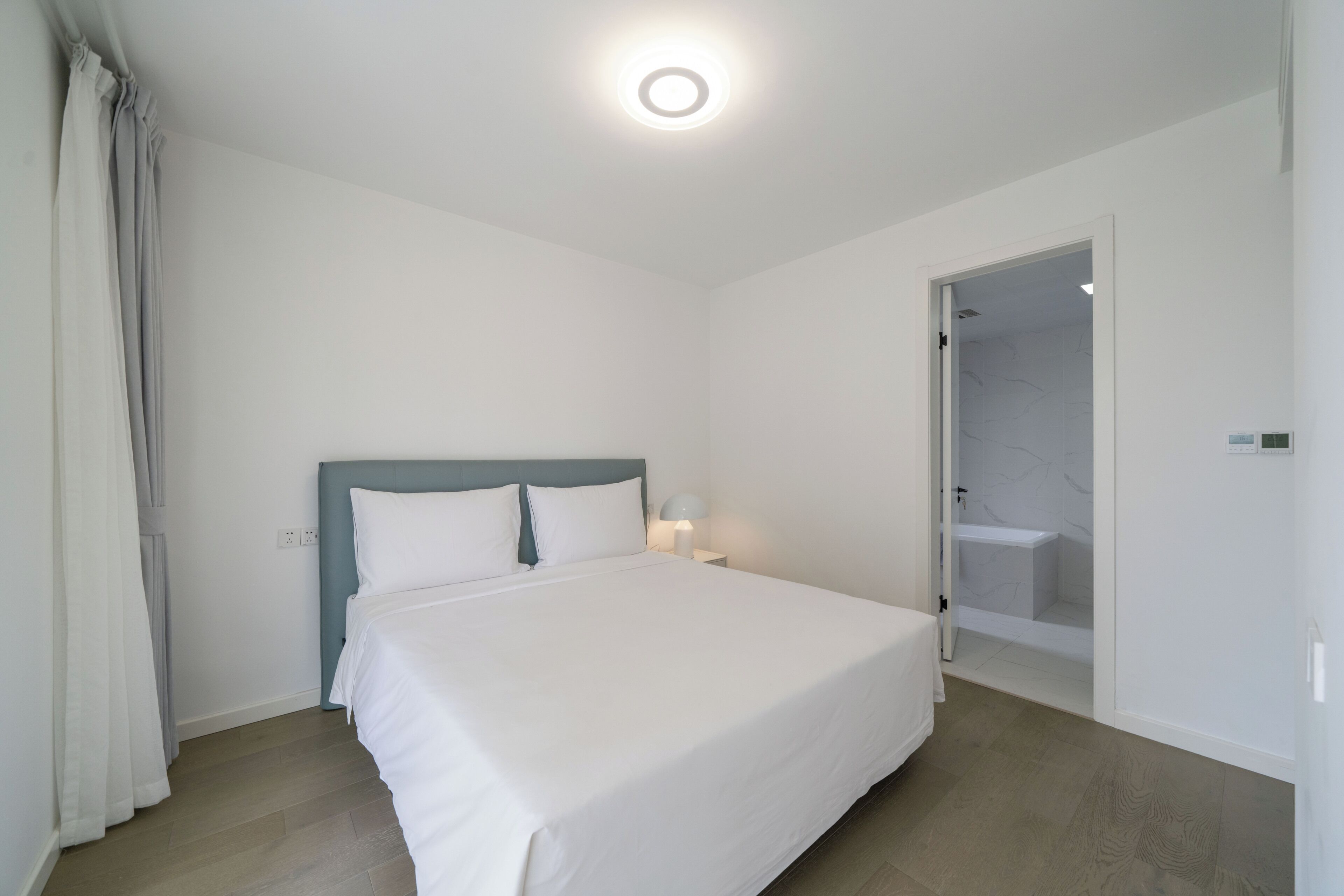 Une chambre à coucher comprenant un lit, une table de chevet, une lampe, une douche et une porte donnant sur une autre pièce.