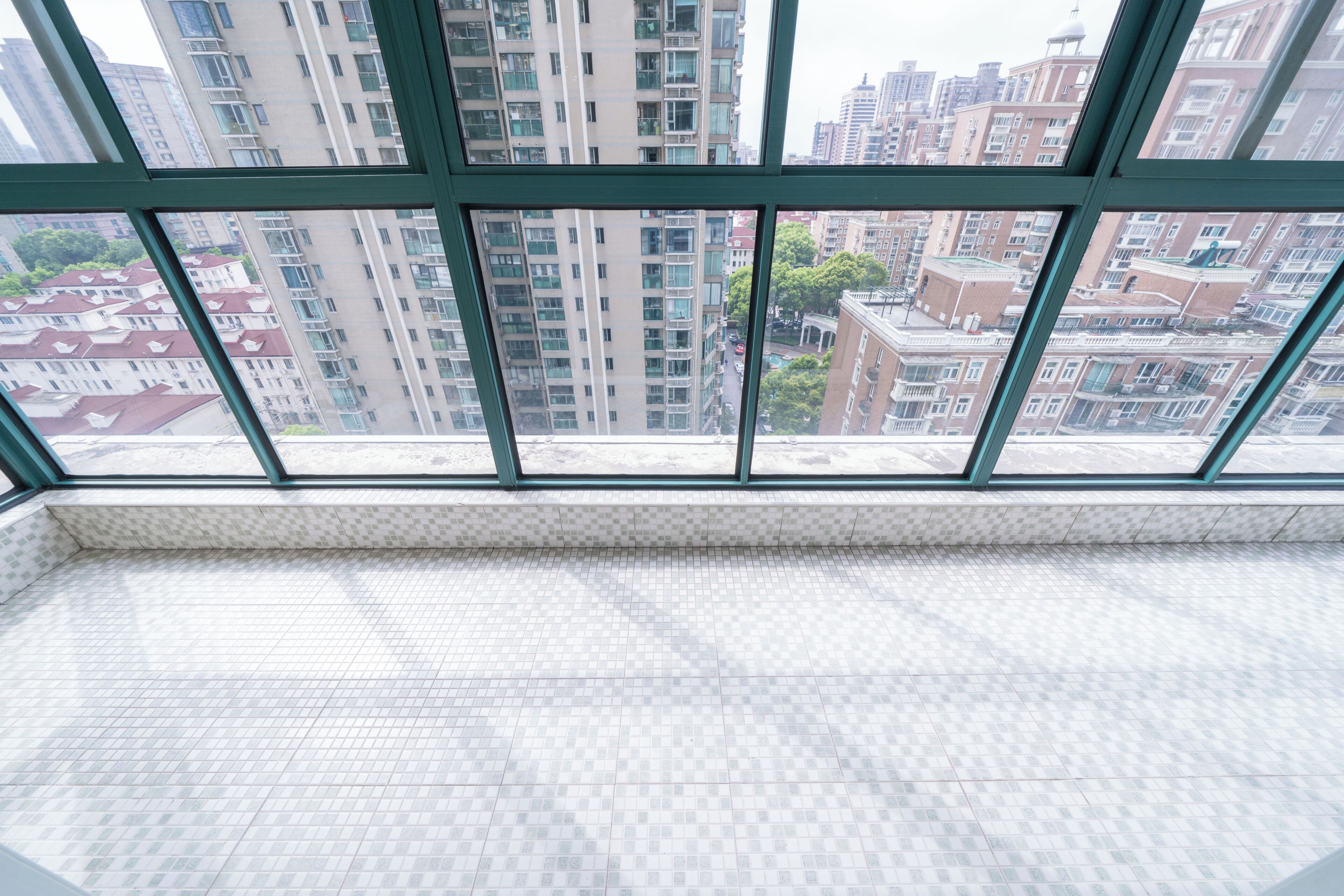 A room with a large window, tiled floor, and a view of high-rise buildings.