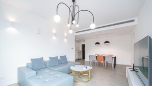 A modern living room with a sectional sofa, a round coffee table, a flat-screen TV, and a dining area with a table and chairs. - Tyms 3BR 2BA Family Serviced Apt (Shanghai)