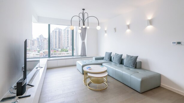A modern living room with a large window, a sofa, a round table, and a flat-screen TV. - Tyms 3BR 2BA Family Serviced Apt (Shanghai)
