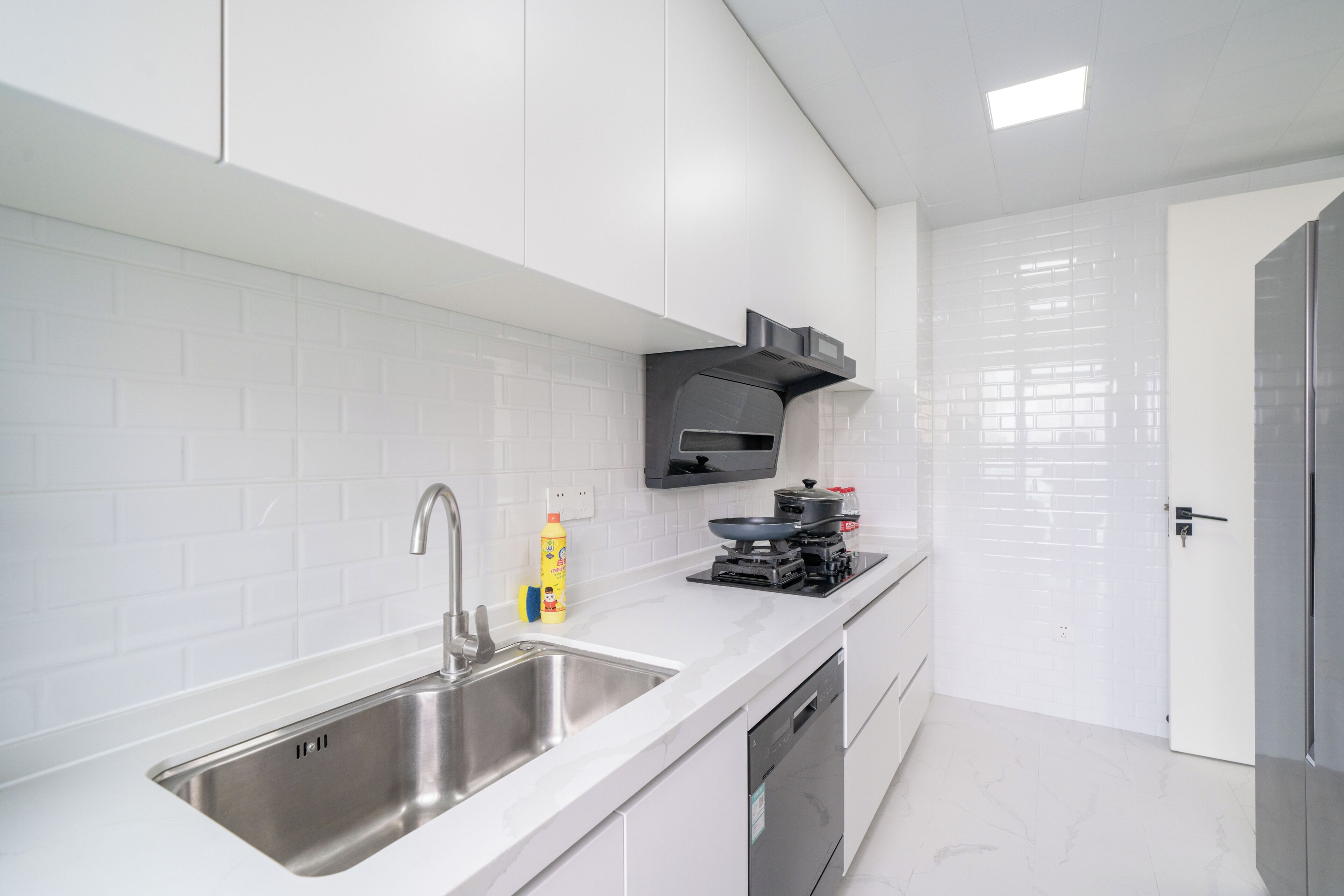 Una cocina moderna con muebles blancos, un lavamanos de acero inoxidable, una estufa integrada y un lavavajillas.