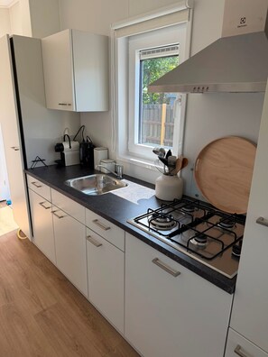 A modern kitchen with white cabinets, a double sink, a gas stove, and a window with a view of the outside.