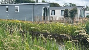 A mobile home with a wooden deck, a small window, and a door. - Chalet 005 (4 persons) (Petten)
