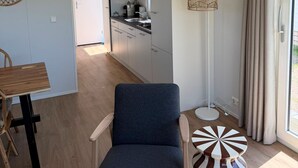 A modern interior with a dining area, a blue chair, a kitchen with white cabinets, and a large window with curtains. - Chalet 005 (4 persons) (Petten)