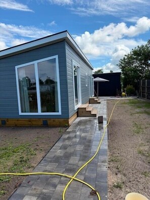 A modern house with a paved patio, a visible water hose, and a covered outdoor area.