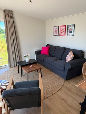 A living room with a dark sofa, a small wooden table, a chair, and a view of the outdoors.