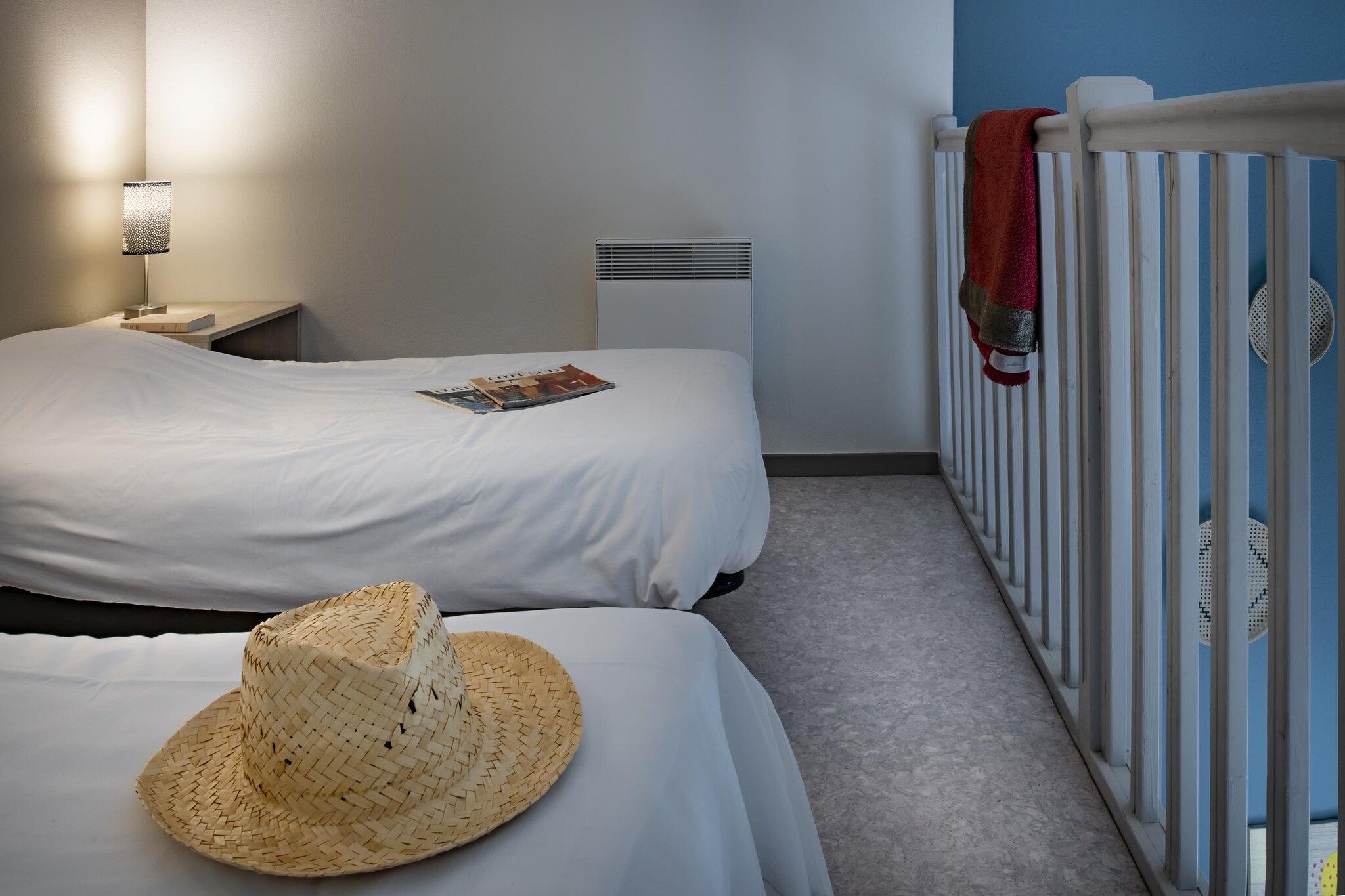 Habitación de hotel con dos camas, una mesita de noche, una lámpara, un radiador y una cuna con una toalla.
