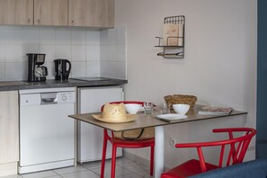 Eine kompakte Küche mit einer Kaffeemaschine, einem kleinen Kühlschrank und einem Essbereich mit Tisch, Stühlen und einem Korb.