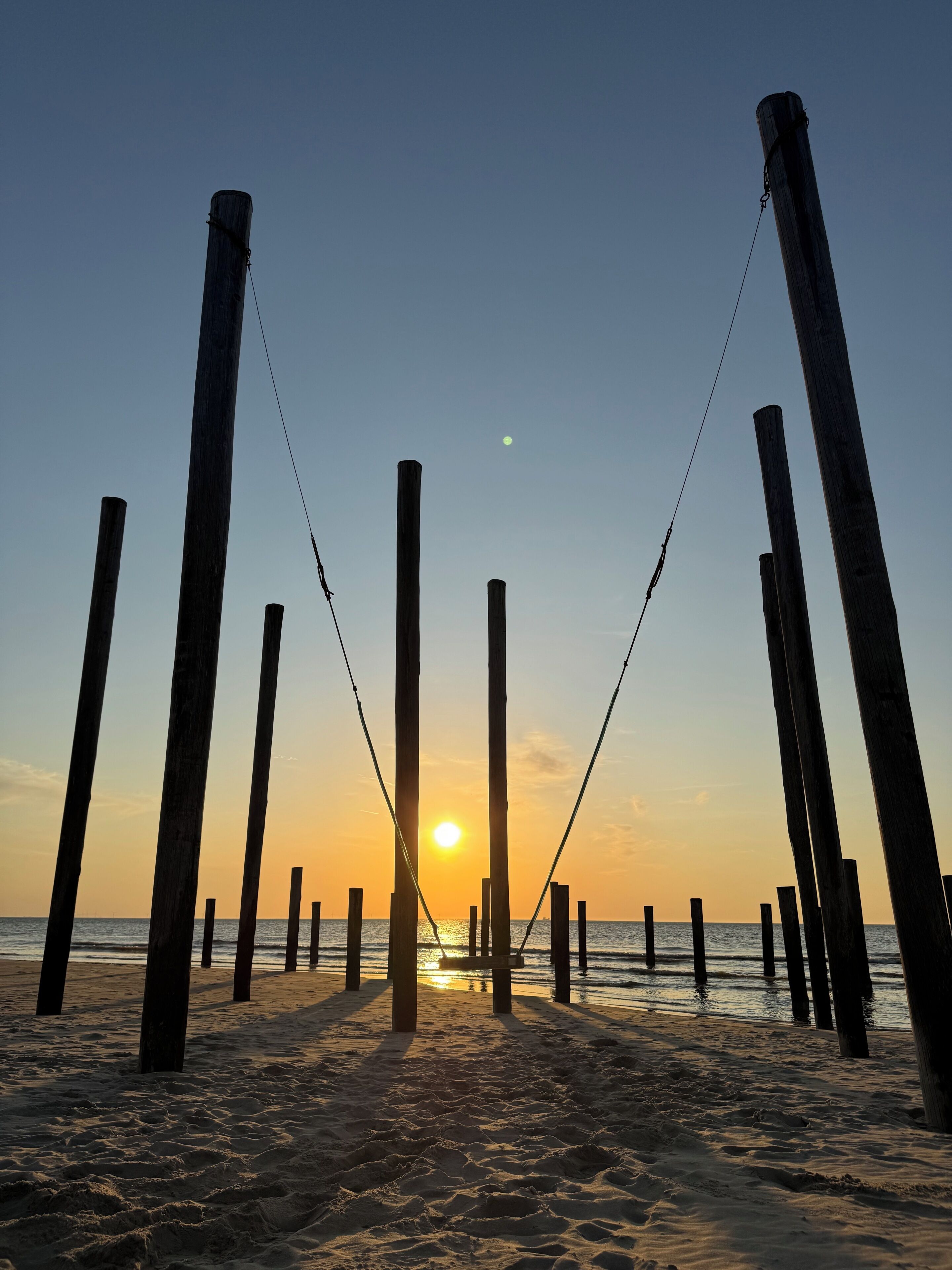 En strand med træpæle og en solnedgang i baggrunden.