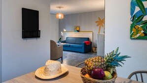 A modern living room with a blue sofa, a dining table with a fruit basket, and a wall-mounted TV. - French Villa with Shared Pool (Fabrègues)