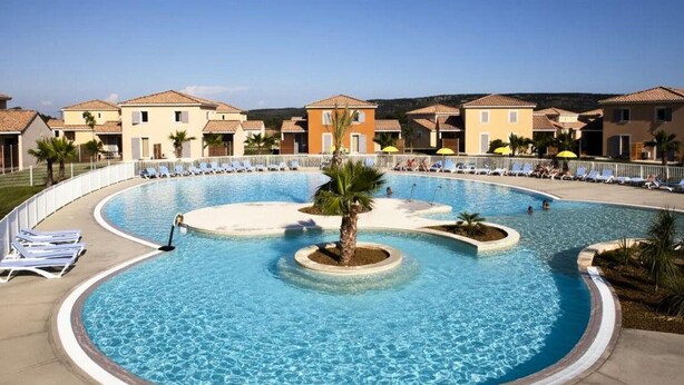 A swimming pool with lounge chairs and palm trees, surrounded by buildings with Mediterranean architecture. - French Villa with Shared Pool (Fabrègues)