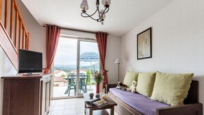 A living area with a sofa, a television, a table with books, and a view of the outdoors. - Lovely Duplex with Scenic Terrace (Carayac)