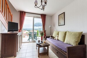 Un espacio de estar con sofá, televisor, una mesa con libros y vistas al exterior.