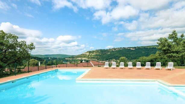 Ein Swimmingpool mit weißen Liegestühlen und Blick auf grüne Hügel.