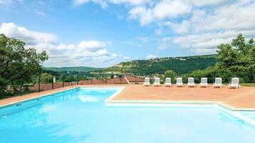 Piscina com espreguiçadeiras brancas e vista para colinas verdes.